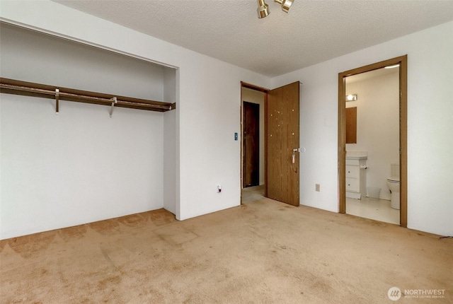 unfurnished bedroom featuring a closet, carpet, ensuite bathroom, and a textured ceiling