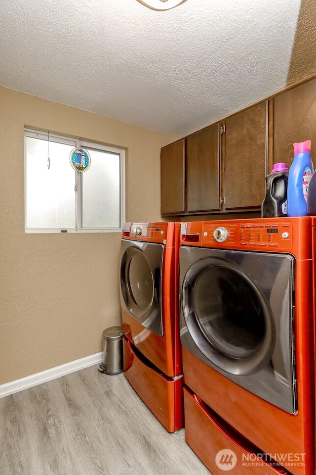 laundry area with baseboards, light wood finished floors, washing machine and clothes dryer, cabinet space, and a textured ceiling