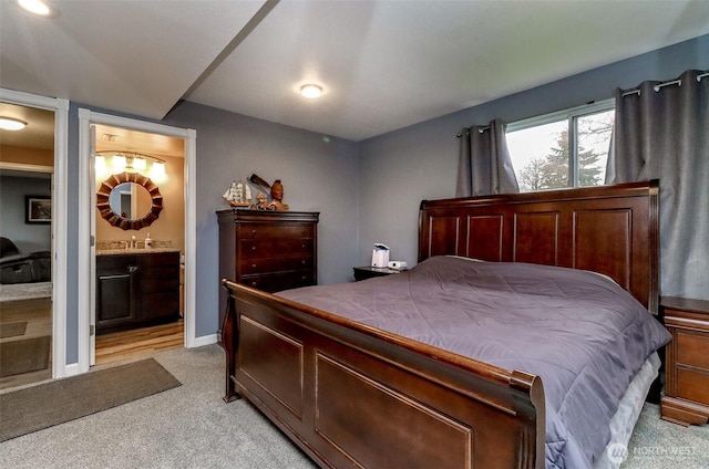 bedroom with a sink, baseboards, light colored carpet, and ensuite bathroom