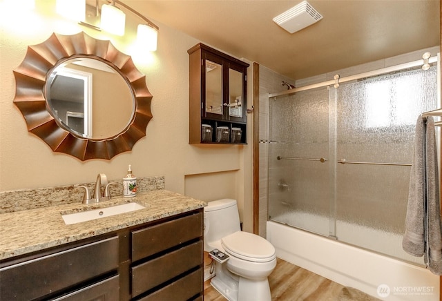 full bathroom with vanity, wood finished floors, visible vents, bath / shower combo with glass door, and toilet