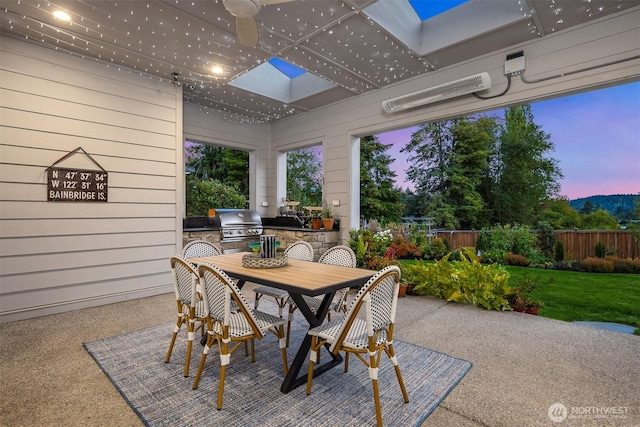 patio terrace at dusk featuring outdoor dining space, a lawn, fence, and area for grilling