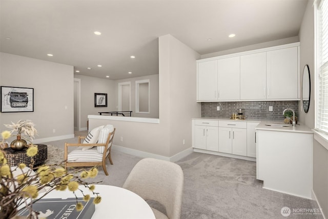 kitchen featuring light carpet, a sink, white cabinets, light countertops, and decorative backsplash