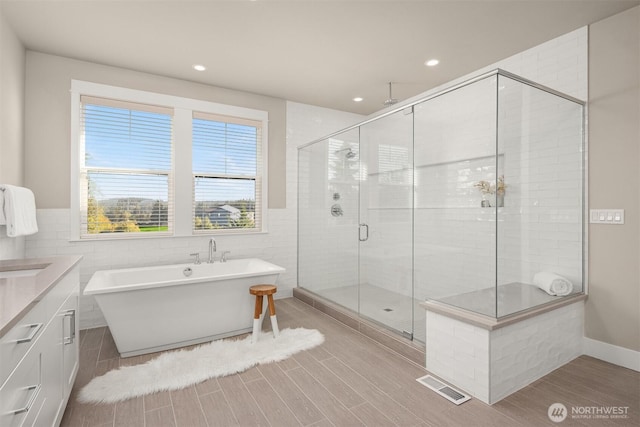 bathroom with visible vents, a stall shower, tile walls, a freestanding bath, and vanity