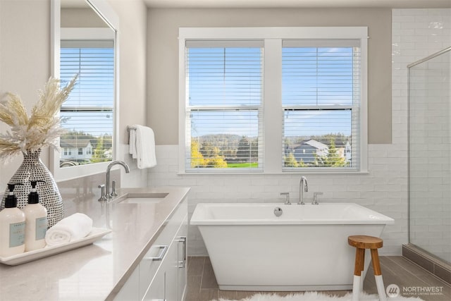 bathroom featuring a freestanding bath, tile walls, vanity, and a tile shower