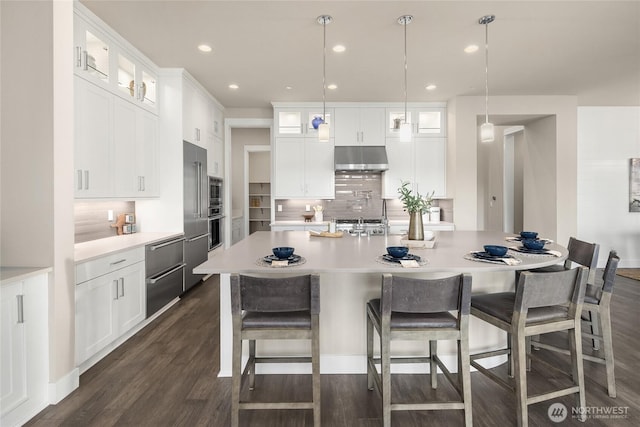 kitchen with under cabinet range hood, backsplash, light countertops, stainless steel oven, and dark wood-style flooring