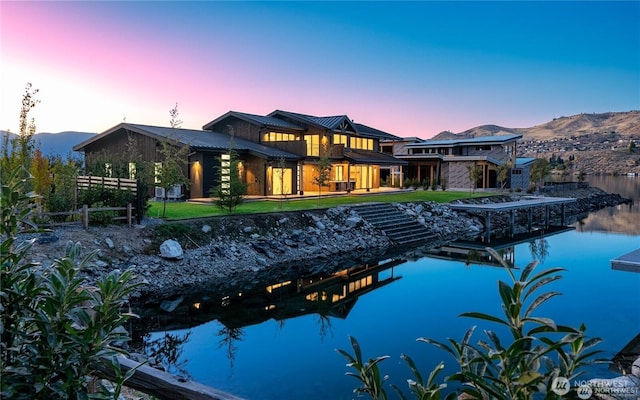 back of house at dusk with metal roof, a water and mountain view, and a lawn