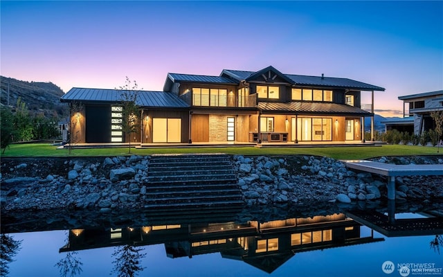 rear view of house with a balcony, a standing seam roof, a water view, a lawn, and metal roof