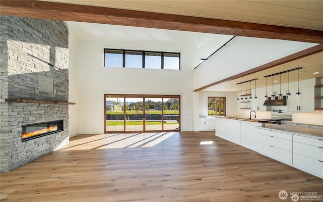 unfurnished living room with a stone fireplace, beam ceiling, wood finished floors, and a sink