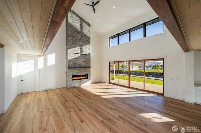 unfurnished living room featuring wood ceiling, high vaulted ceiling, a stone fireplace, and wood finished floors