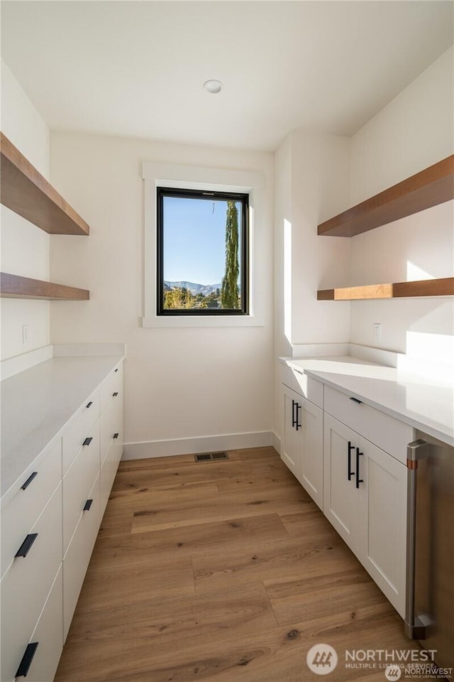 interior space with baseboards, visible vents, open shelves, light wood-style flooring, and white cabinetry