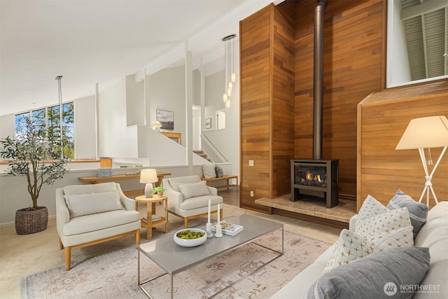 carpeted living area with stairs, high vaulted ceiling, and a wood stove