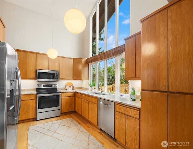 kitchen featuring light wood-type flooring, a sink, stainless steel appliances, a towering ceiling, and brown cabinets