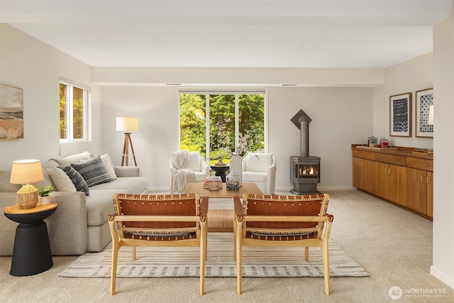 dining space featuring light colored carpet, a wood stove, and baseboards