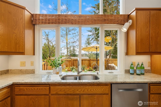 kitchen featuring light stone counters, plenty of natural light, brown cabinets, and a sink