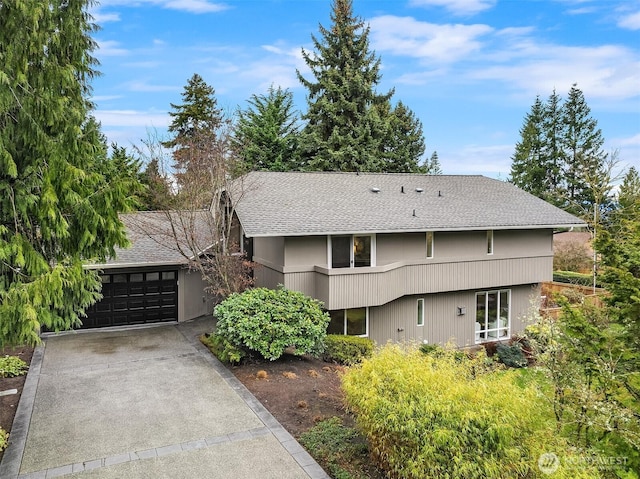 exterior space with concrete driveway, an attached garage, and a shingled roof