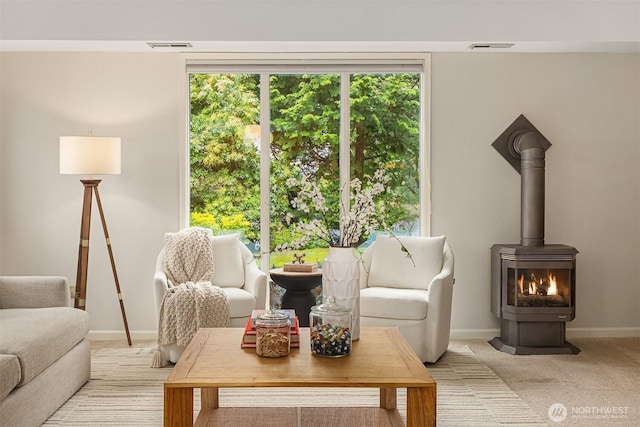 living area with a wood stove, light colored carpet, visible vents, and baseboards