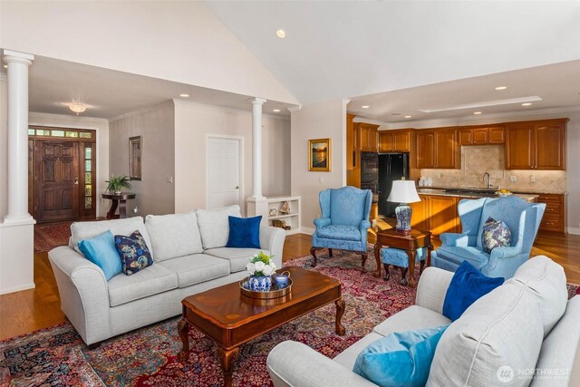 living area featuring light wood-style floors, ornamental molding, high vaulted ceiling, and ornate columns