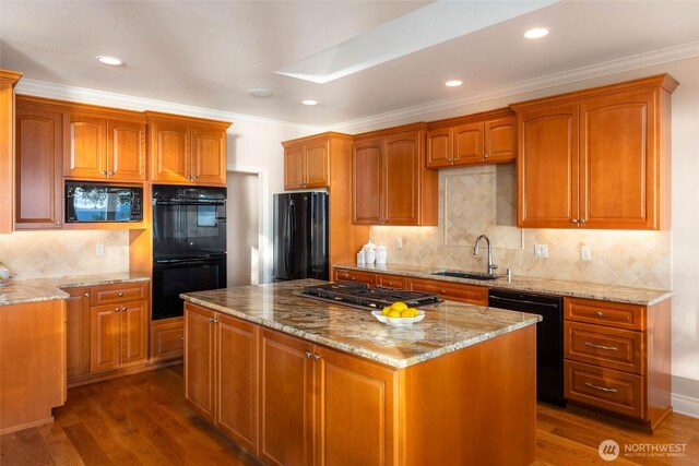 kitchen featuring a center island, dark wood finished floors, light stone counters, black appliances, and a sink