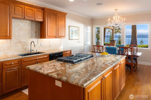 kitchen with a sink, light stone counters, black dishwasher, wood finished floors, and crown molding