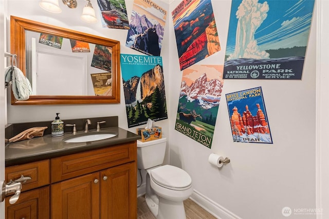 half bathroom featuring vanity, toilet, wood finished floors, and baseboards