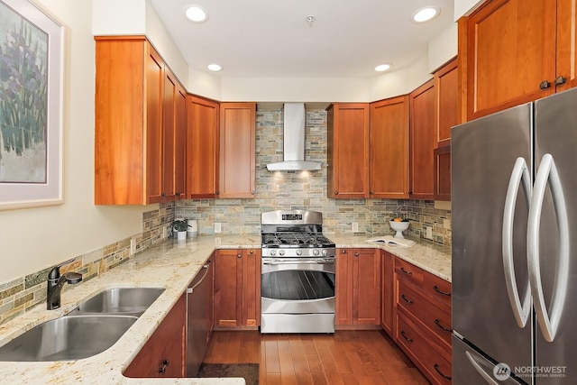 kitchen with a sink, backsplash, appliances with stainless steel finishes, wall chimney exhaust hood, and light stone countertops