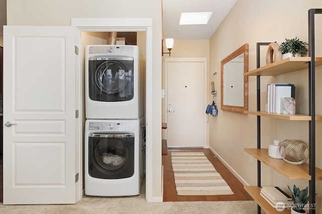 clothes washing area with baseboards, stacked washer and clothes dryer, a skylight, and laundry area