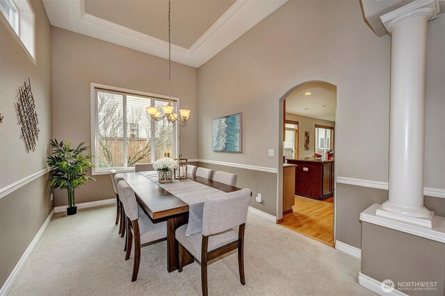 dining space featuring light carpet, arched walkways, baseboards, and decorative columns