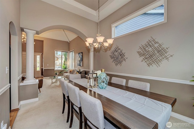 dining room featuring decorative columns, baseboards, light colored carpet, and arched walkways