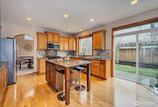 kitchen with arched walkways, a sink, stainless steel appliances, light wood-style floors, and a kitchen bar