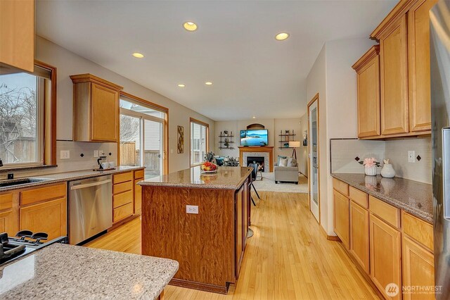 kitchen featuring light wood finished floors, open floor plan, a kitchen island, and stainless steel dishwasher