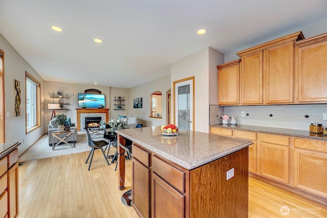 kitchen featuring light wood-type flooring, a kitchen island, open floor plan, a lit fireplace, and decorative backsplash