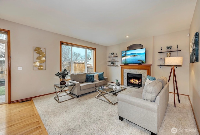 living area featuring a high end fireplace, visible vents, baseboards, and light wood-style floors