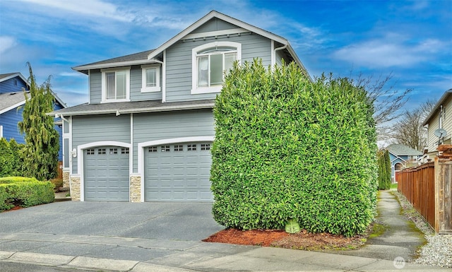 view of side of property featuring a shingled roof, fence, concrete driveway, stone siding, and an attached garage