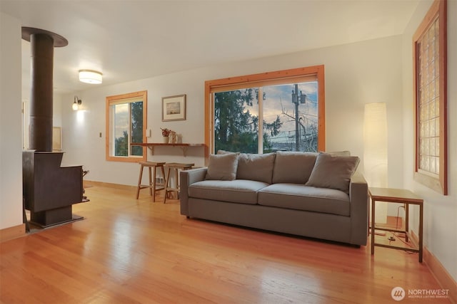 living area featuring light wood-style flooring, baseboards, and a wood stove