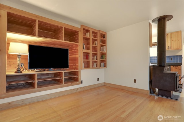 living area with light wood-type flooring, baseboards, and a wood stove