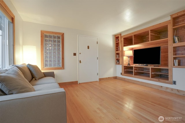 living area with built in features, baseboards, and light wood-type flooring