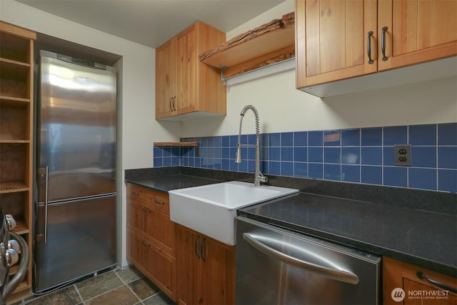 kitchen with stone finish floor, a sink, dark countertops, appliances with stainless steel finishes, and decorative backsplash