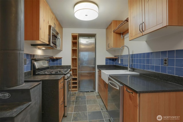 kitchen featuring dark countertops, backsplash, stone finish floor, stainless steel appliances, and a sink