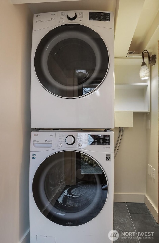 laundry room with laundry area, stacked washer / dryer, dark tile patterned floors, and baseboards