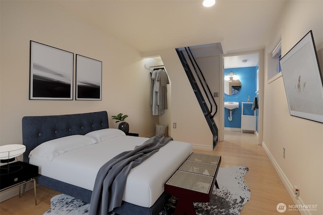 bedroom with connected bathroom, light wood-type flooring, baseboards, and a sink