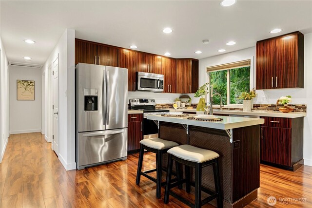 kitchen featuring a sink, dark wood-type flooring, light countertops, appliances with stainless steel finishes, and a kitchen breakfast bar