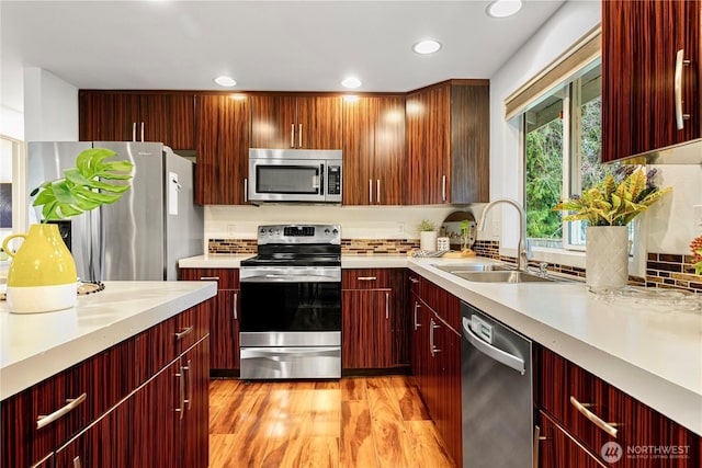 kitchen featuring light wood finished floors, a sink, stainless steel appliances, light countertops, and reddish brown cabinets