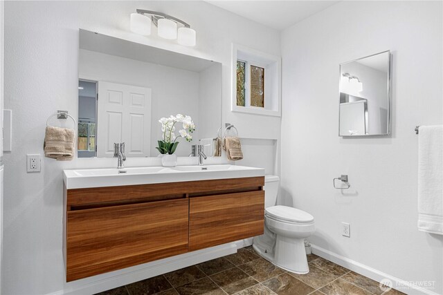 full bath with double vanity, toilet, baseboards, and a sink