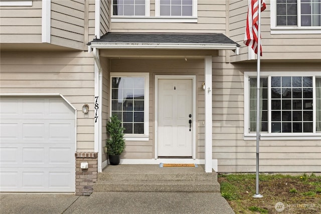 entrance to property featuring an attached garage and a shingled roof