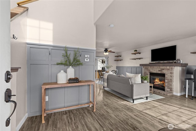 living area featuring a ceiling fan, a brick fireplace, a decorative wall, and wood finished floors