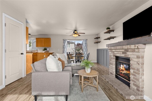 living area with a healthy amount of sunlight, a brick fireplace, light wood-type flooring, and a ceiling fan