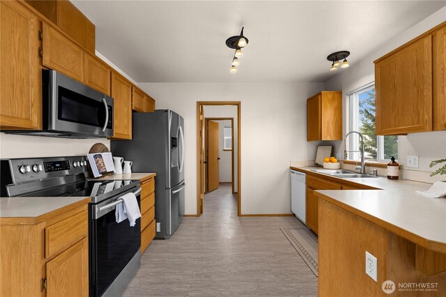 kitchen featuring baseboards, light countertops, brown cabinets, appliances with stainless steel finishes, and a sink