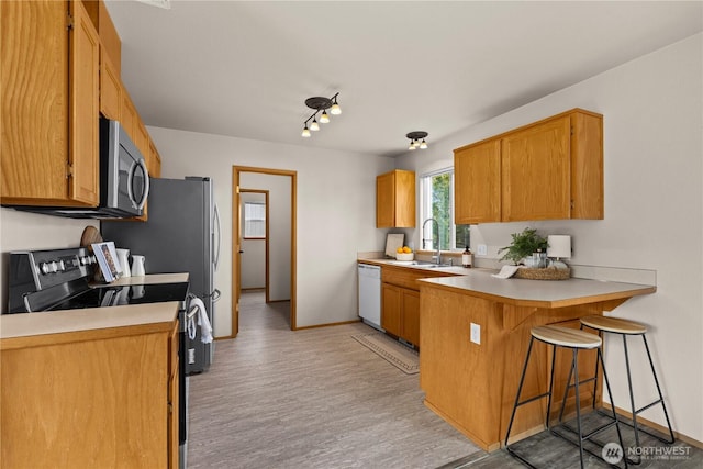 kitchen featuring stainless steel microwave, a peninsula, a kitchen breakfast bar, electric stove, and a sink