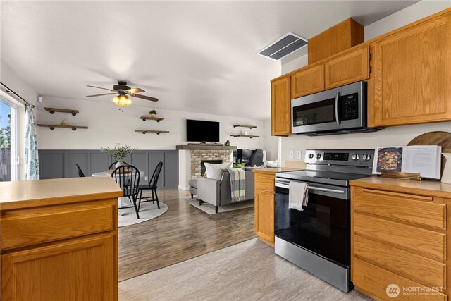 kitchen featuring visible vents, open floor plan, light wood-style flooring, a fireplace, and stainless steel appliances