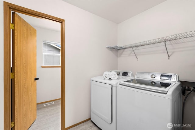 clothes washing area featuring baseboards, visible vents, washing machine and clothes dryer, laundry area, and light wood-style floors